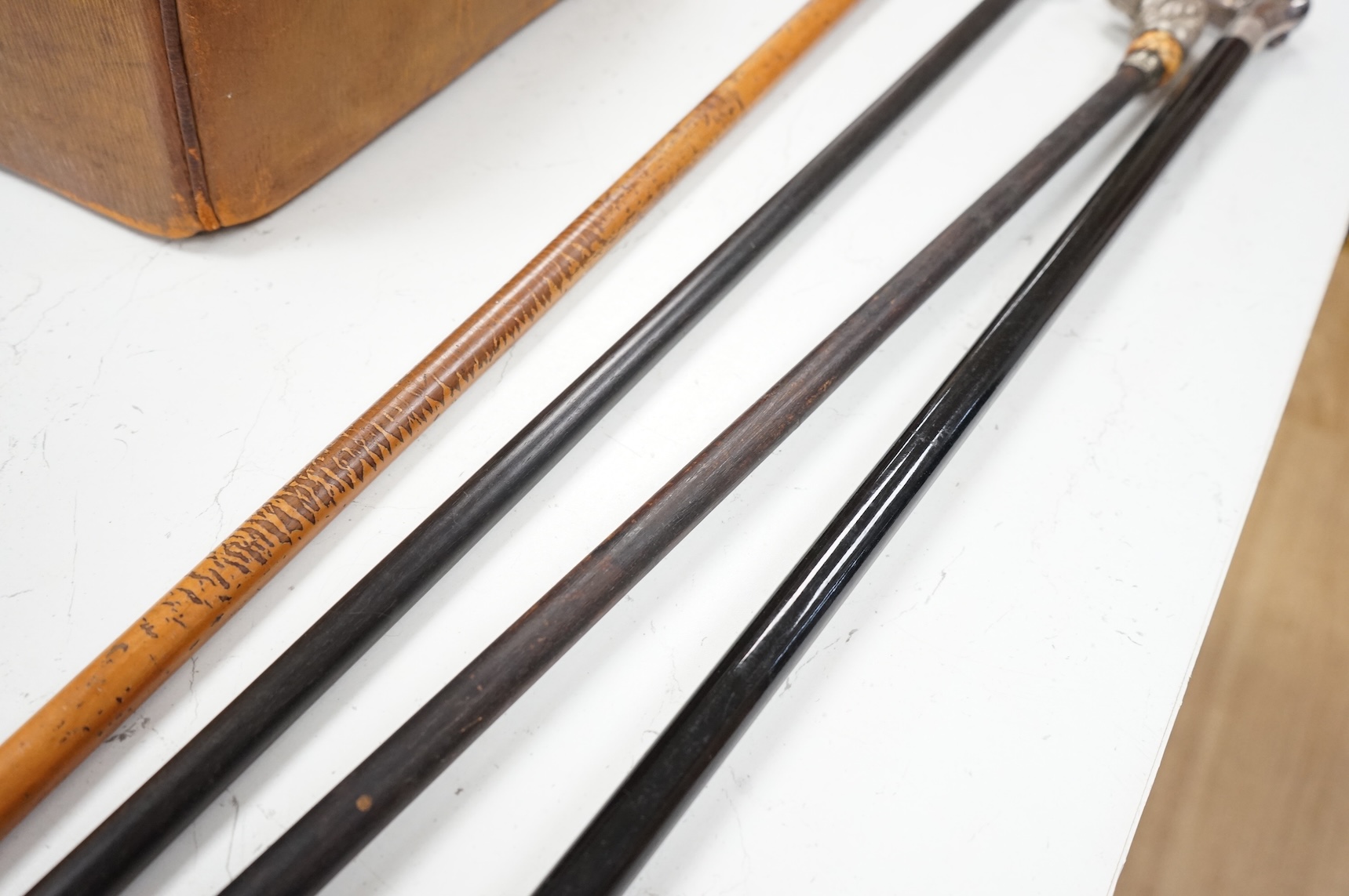 Four 19th century and later walking sticks with silver and white metal tops, to include three horse racing interest examples, largest 96cm in length
